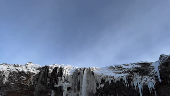 Tilt down shot of spectacular icy Seljalandsfoss Waterfall in winter during sunlight