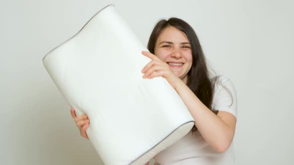 Happy Brunette Woman Dancing with Her Favorite Orthopedic Pillow on a White Background