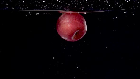 Colorful red apple being dropped into water in slow motion.