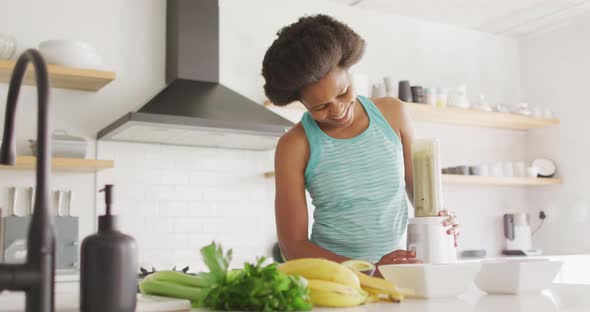 Happy african american woman preparing healthy drink in kitchen