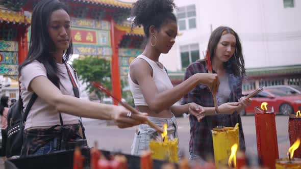 A group of multi-ethnic female friends praying at a Chinese shrine in Bangkok, Thailand.