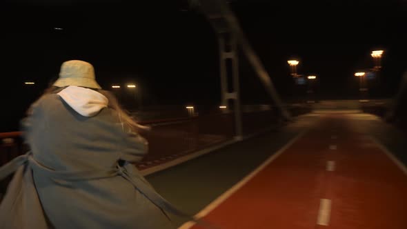 Modern Girl Dancing at Night on the Bridge Against the Background of a Big City