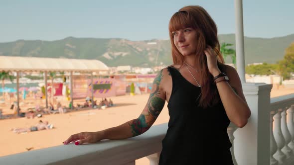 Tanned young smiling woman with a sleeve tattoo, posing near stone ballustrade