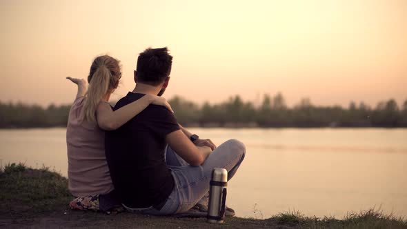 Couple On Sunset.Couple Relaxing On River. Lovers Sitting On Sunset..Happy Couple In Love