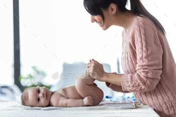 Smiling young mother has fun with little baby while changing his nappy at home.