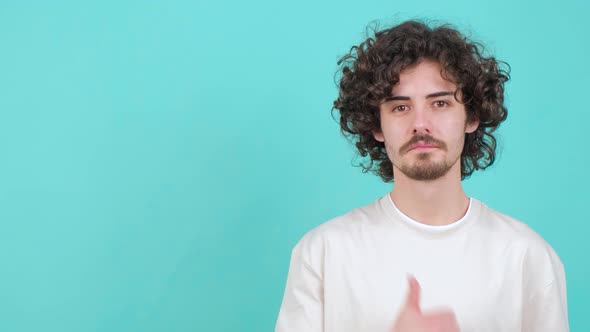 Young Curly Haired Man is Pointing to the Right and Showing the Thumb Up Gesture