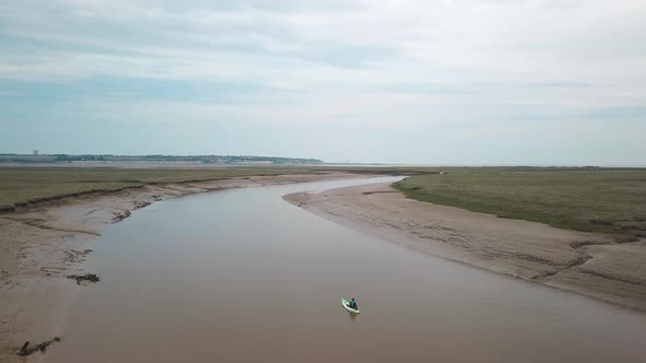 Man kayaking on meandering river, drone pans to the right with beautiful landscape in the background