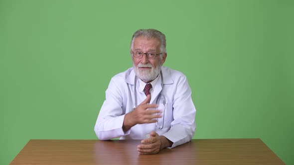 Handsome Senior Bearded Man Doctor Against Green Background