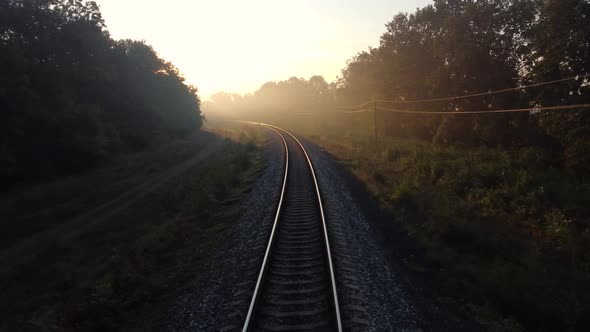 The train road is covered with morning fog, sunlight through tree branches and long shadows.