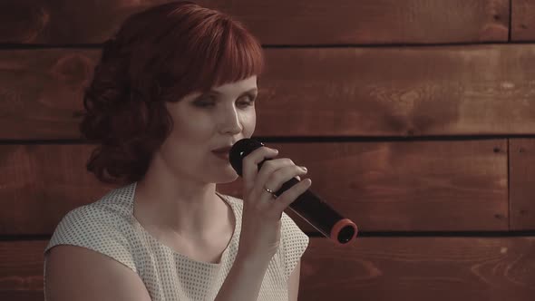 Young Girl Speaks Into Microphone Against a Background of Wooden Boards Closeup