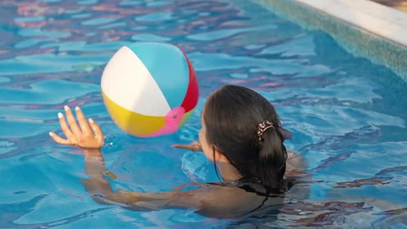 A Girl in a Bright Bathing Suit Swims with an Inflatable Ball in a Pool with Clear Water on a Summer