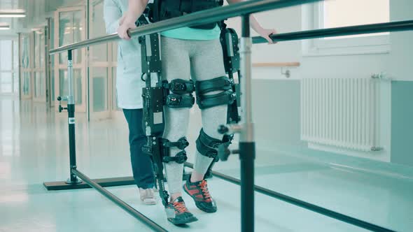 A Patient in Exoskeleton is Being Assisted By a Doctor While Walking