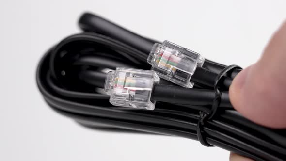 Bundle of a new black telephone cable with plugs in a hand on a white background