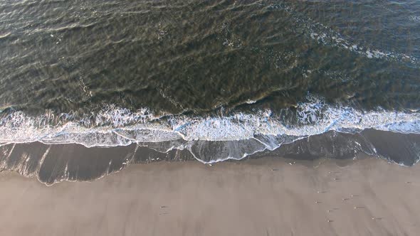 Aerial, static, drone shot of calm waves hitting a beach, on Langeoog island, on a sunny day, in Nor