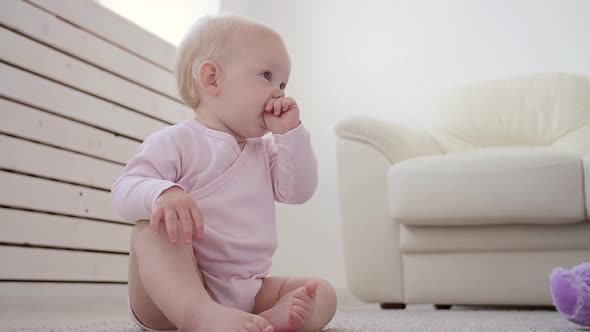 Childhood, Babyhood and Family Concept - Happy Little Baby Boy or Girl Sitting on Floor at Home