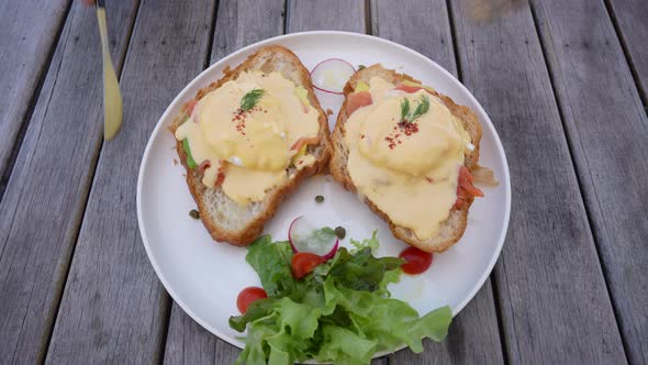 Croissant sandwich with poached egg, radish and salmon on plate in cafe