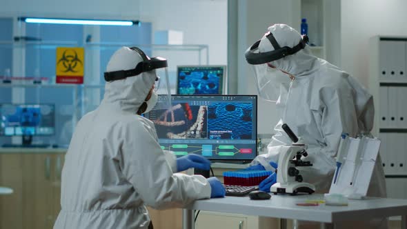 Scientists in Protection Suits Analysing Test Tubes with Blood Sample