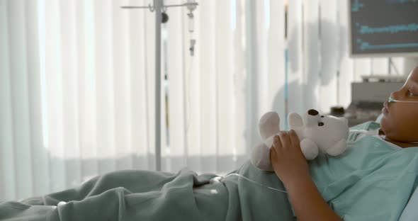 Side View of Cute African Girl Lying in Hospital Bed with White Teddy Bear