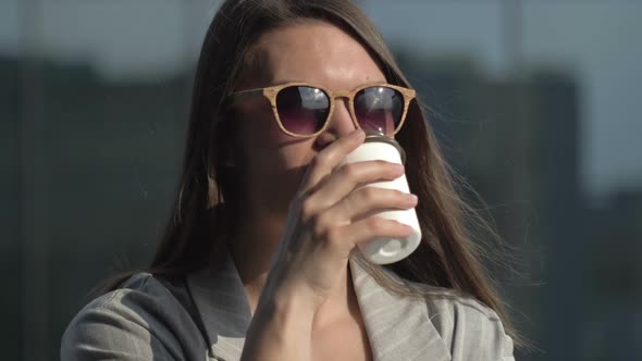 Smiling Young Woman in Sunglasses Drinks Coffee From a Disposable Cup