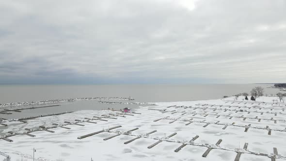 Drone view over frozen and snow covered marina with empty boat slips. Cloudy winter sky.