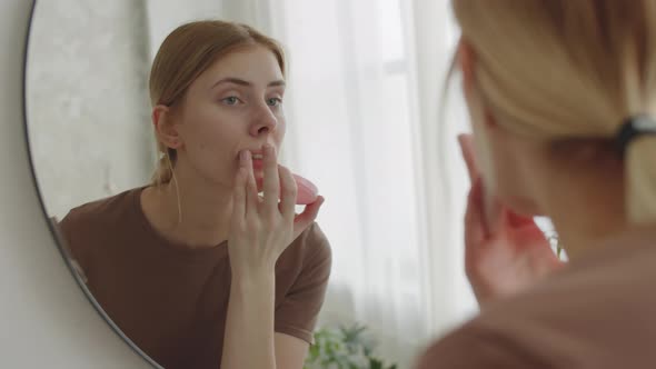 Young Pretty Woman Applying Cream to Face in Bathroom