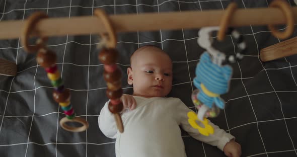 Little Newborn Baby Boy Lies Under Foldable Wooden Montessori Fitness Baby Gym