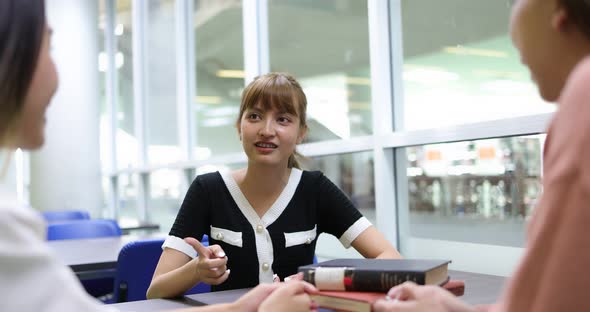 Smiling Asian student female  meeting with groupmates, explaining new project detail in library.