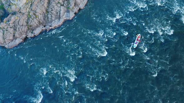 Aerial View of a Kayak Boat Rushing Along a Turbulent River Between Stone Rocks at High Speed