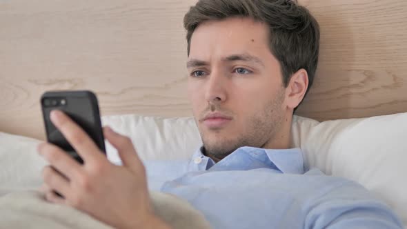 Young Man Using Smartphone in Bed