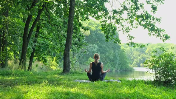 Beautiful free woman sitting in meditation pose in green forest. Lotus position, zen yoga meditation