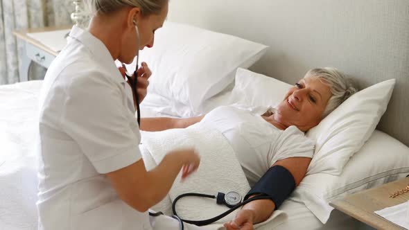 Female doctor checking the blood pressure of senior woman in the bedroom