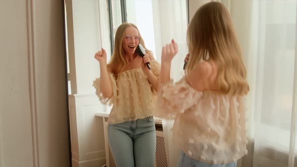 A young woman sings into a hairbrush as like microphone in front of a mirror dance