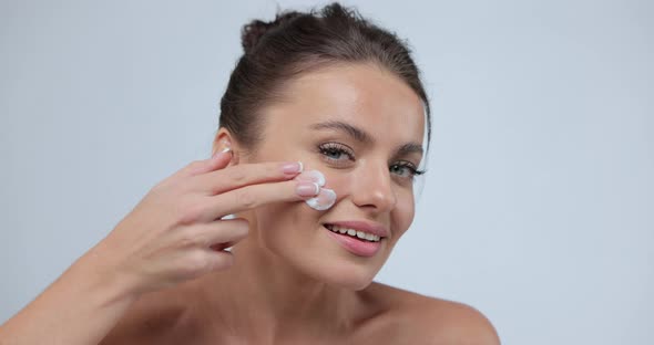 Young Woman Putting Cream on Her Chick and Laughing to Camera Pretty Female Model Using Cosmetics