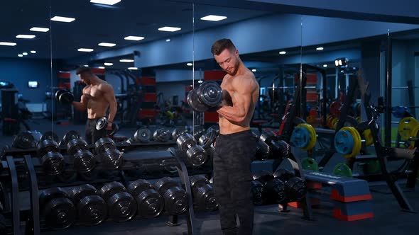 Athletic shirtless young male fitness model holds the dumbbell