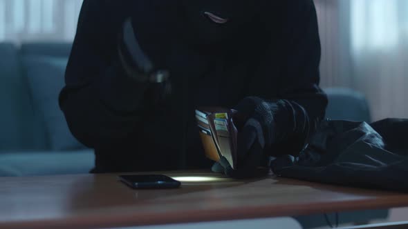 Close Up Of A Thief Man Holding Flashlight Stealing Wallet And Smartphone In Someone'z House