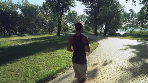 A Young Male in Headphones and Sportswear Runs a Summer Day, Green Trees