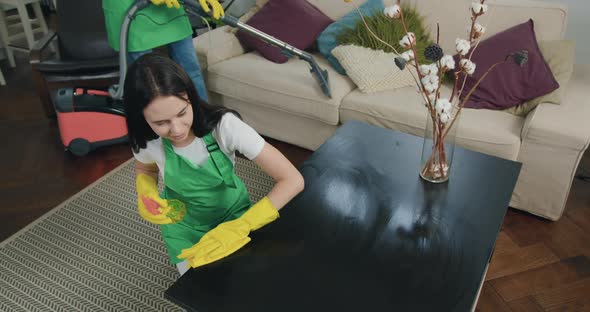 Woman-Cleaner in Apron and Gloves which Wiping Wooden Table with Detergent