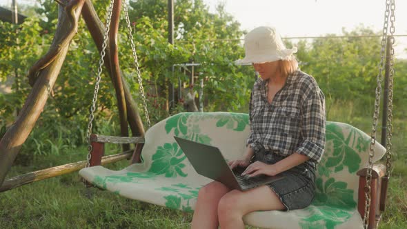 Young adult woman working outdoors in her garden with laptop. Freelancer using laptop computer