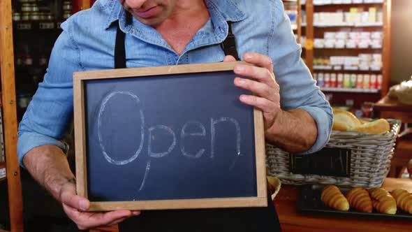 Male staff holding a open sign slate in supermarket