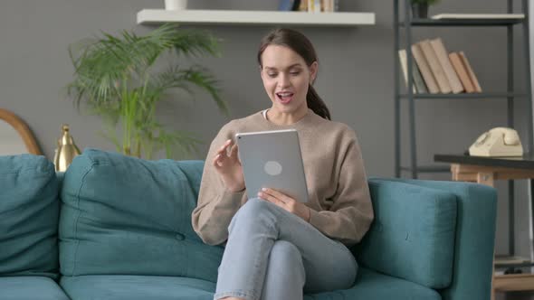 Woman Celebrating Success on Tablet on Sofa