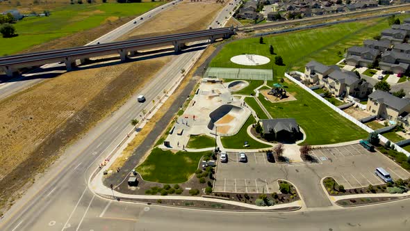 orbiting aerial view of a skate park between a highway and a suburban neighborhood