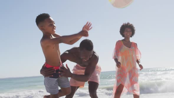 Smiling african american family playing with ball on sunny beach