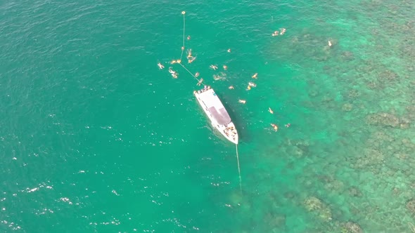 drone shots of groups of people swimming near their boat in crystal clear waters