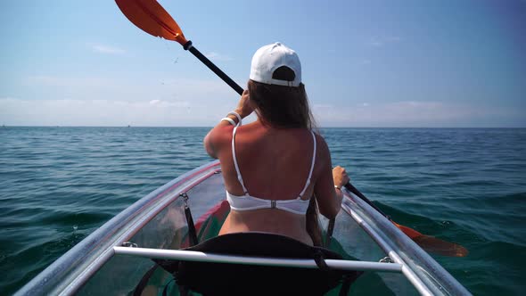 Young Attractive Brunette Woman with Long Hair in White Swimsuit Swimming on Transparent Kayak