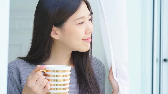 beautiful asian female woman enjoy freshness morning time with hot drink coffee in bedroom with wind