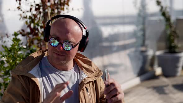 Closeup of the Face of a Happy Bald Man with Crystal Glasses in Headphones Listening to Music Using