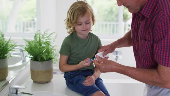Caucasian grandfather helping his grandson to apply toothpaste on toothbrush at home