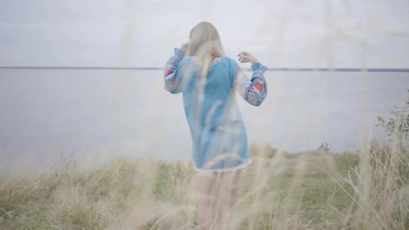 Attractive Blond Girl in Beautiful Short Blue Summer Dress with Embroidery Dancing on the Grass