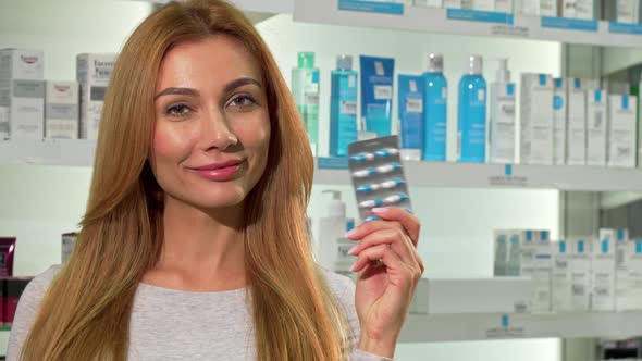 Lovely Happy Woman Holding Blister of Pills, Smiling at the Pharmacy