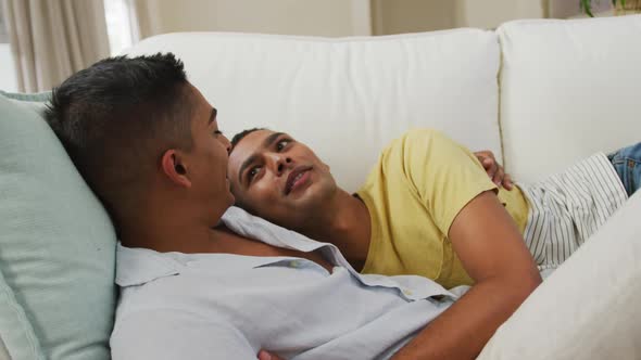 Smiling mixed race gay male couple hugging lying on sofa together